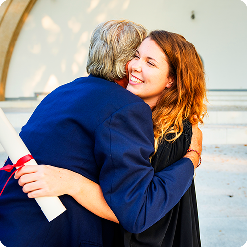 A father in a blue suit hugging his daughter in her gown as she graduates.