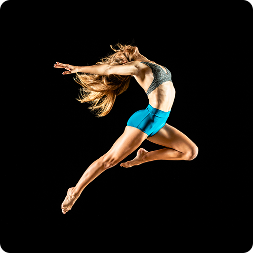 A dance photography sample of a woman in a blue outfit leaping into the air, dramatically lit in front of a black background.