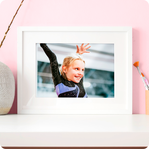 A photo frame on a desk displaying a picture of a young female gymnast smiling.