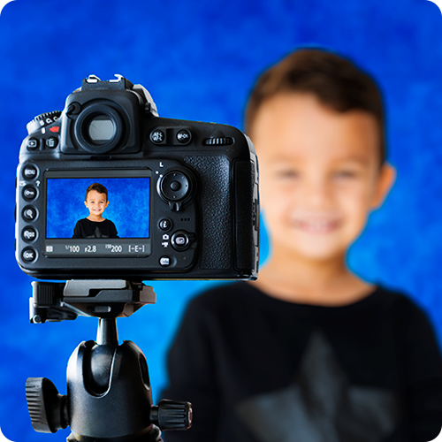 A camera in the foreground for school photo day, with a boy on the screen smiling as his picture is being taken. The same boy is shown in the background, out of focus.