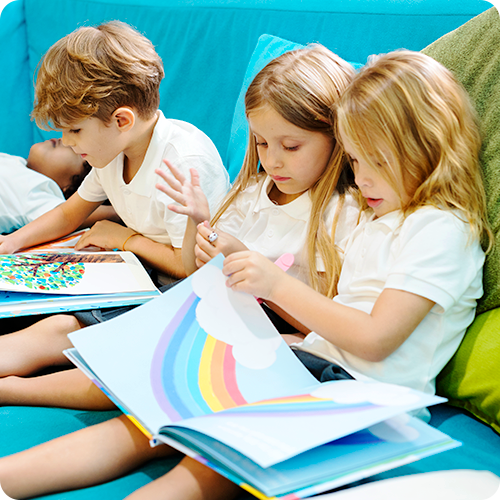 Two girls and two boys of an elementary school age on a blue sitting area, reclining back and reading picture books.